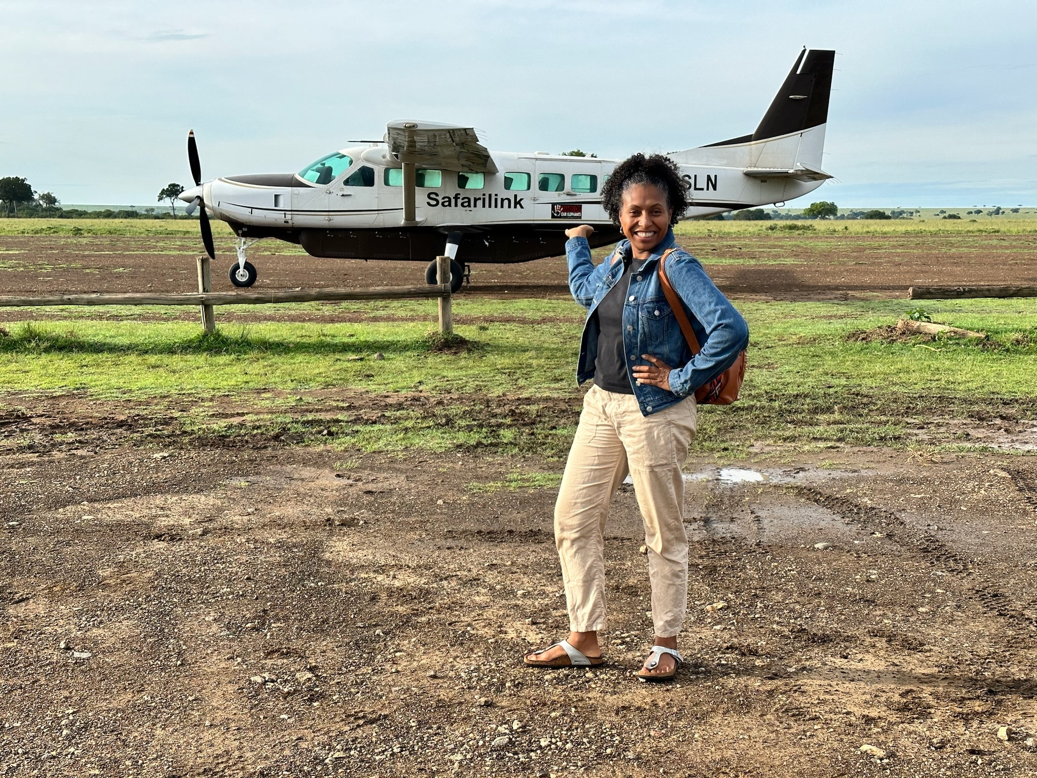 Noelle from Pockets of Orange smiling happy standing in front of a propeller plane in Africa.